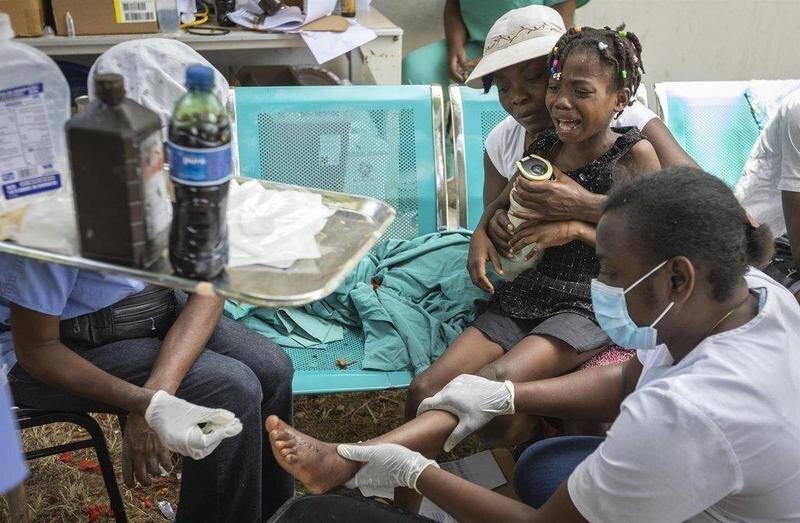  16 August 2021, Haiti, Les Cayes: A young girl is held by her mother as nurses care for a wound on her foot at OFATMA Hospital, as the patients afraid of hospital collapse after it's walls and floor cracked during the earthquake. Rescuers in Haiti are wor - Jose A. Iglesias/TNS via ZUMA Pr / DPA 