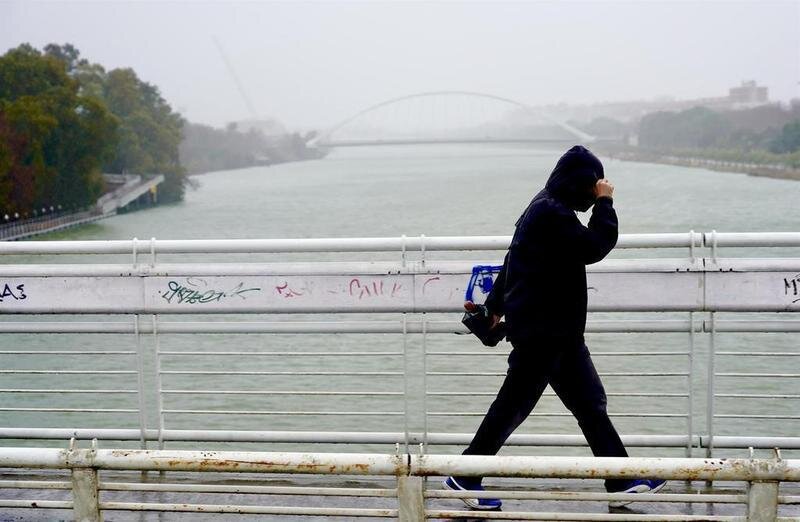 <p> Imagen de archivo de un persona protegiéndose de la lluvia y el viento en Sevilla </p>