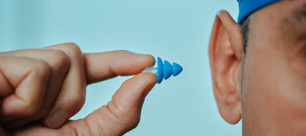  a swimmer man, wearing a blue swimming cap, is about to put an earplug, in a swimming pool, in a panoramic format to use as web banner or header 